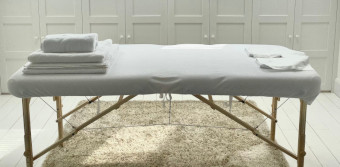 A white massage table with white towels in a clean bright room bright with light flooding in through skylights.